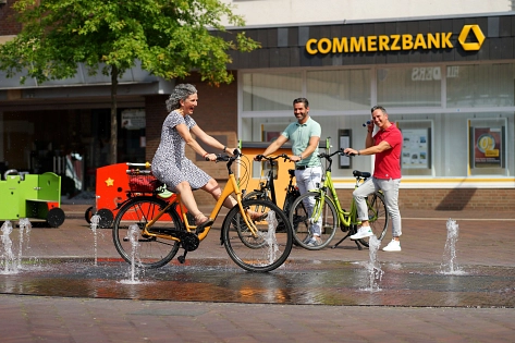 Eine Radfahrerin fährt mit dem Fahrrad durch das Wasserspiel in der Meppener Innenstadt.
