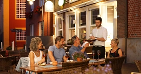 Vier Personen sitzen in einem Restaurant, ihnen werden gerade Getränke serviert.