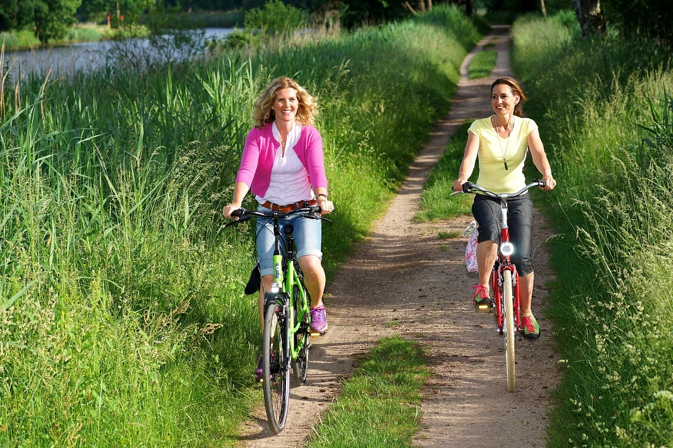 Zwei Radfahrerinnen radeln durch die Natur entlang eines Flusses.
